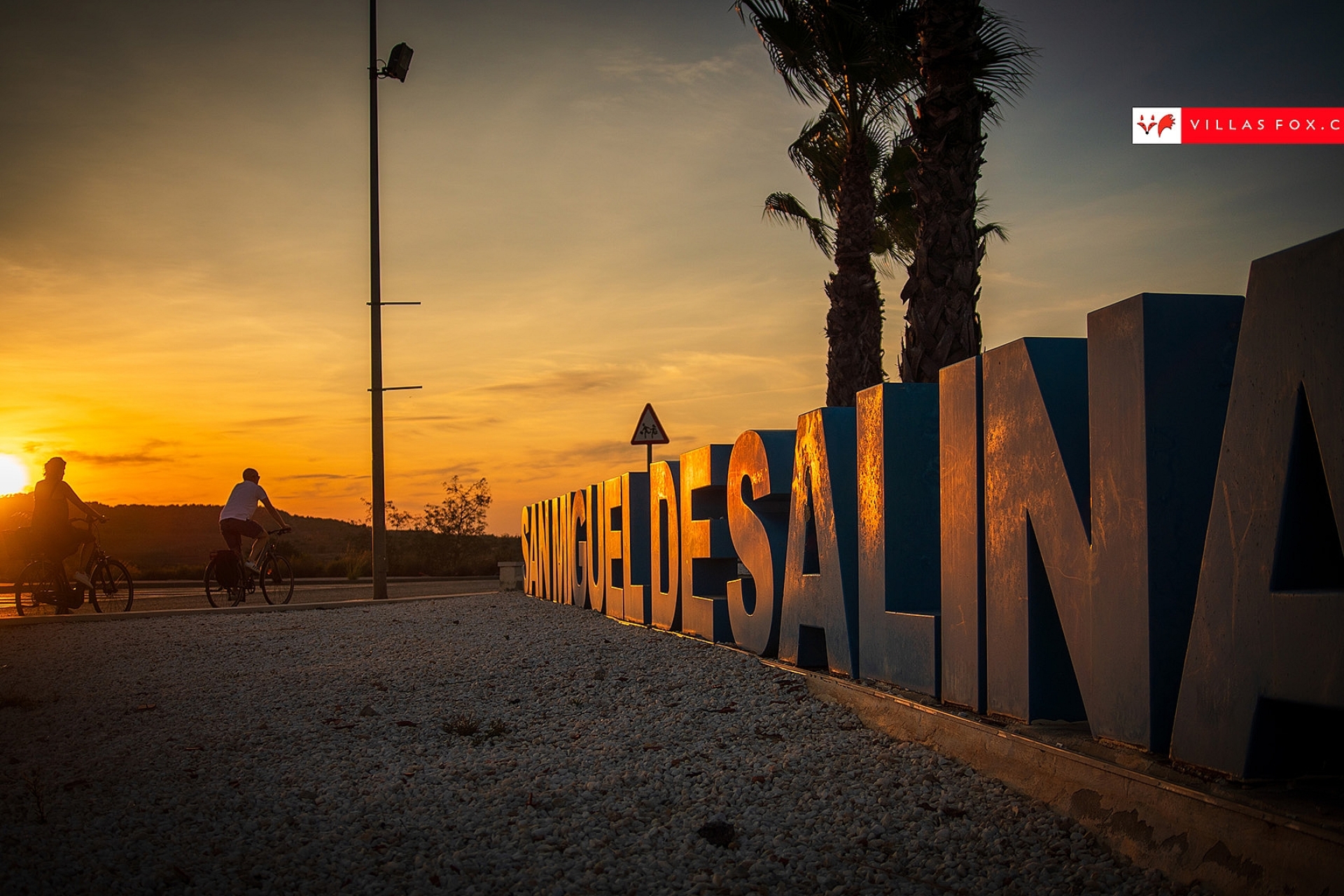 San Miguel de Salinas cyclists and town sign at sunset