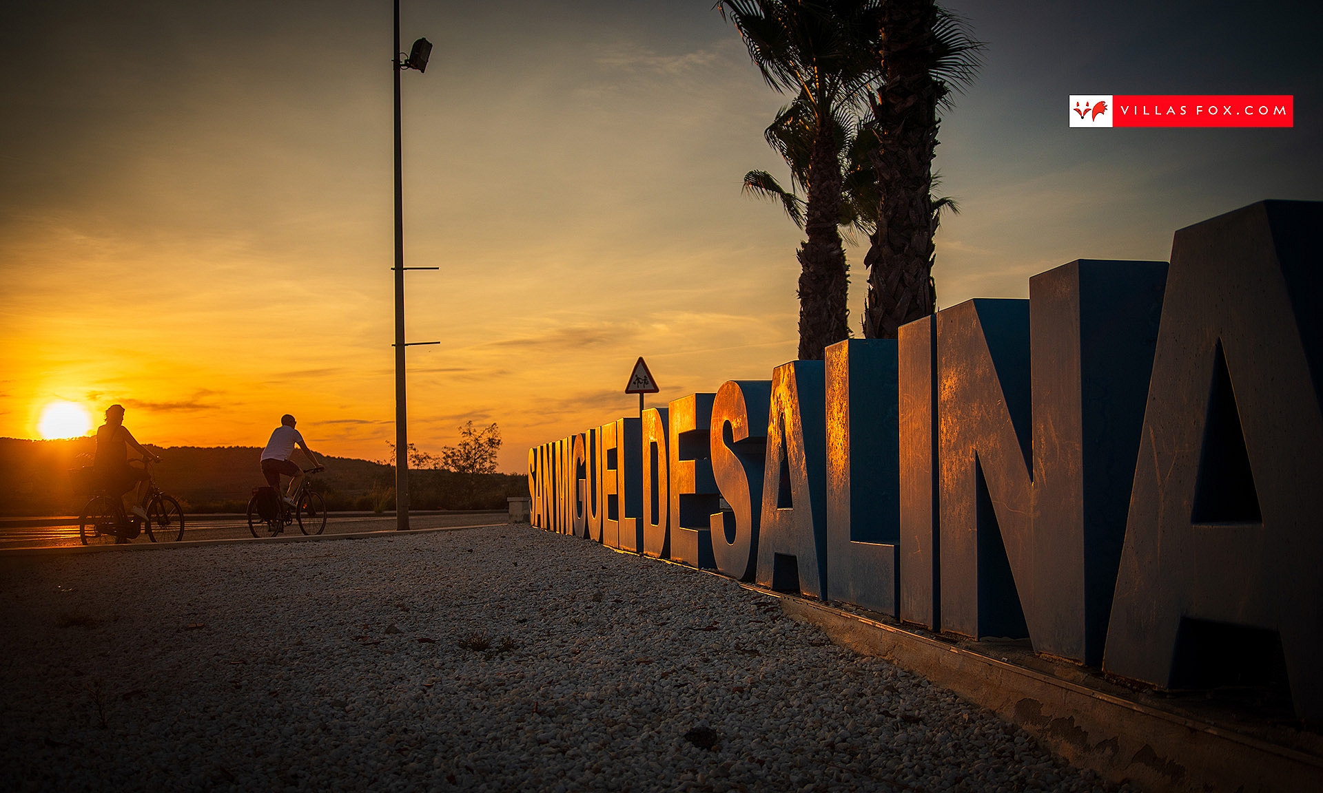 San Miguel de Salinas cyclists and town sign at sunset